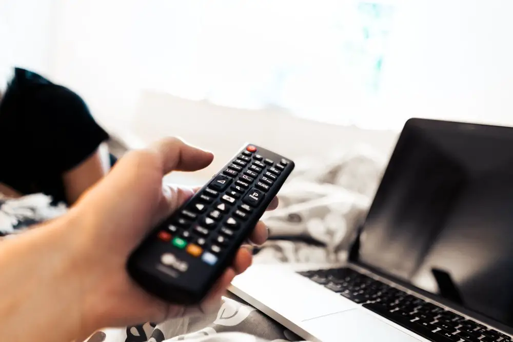 Person pointing a TV remote at a laptop to represent movie streaming affiliate programs
