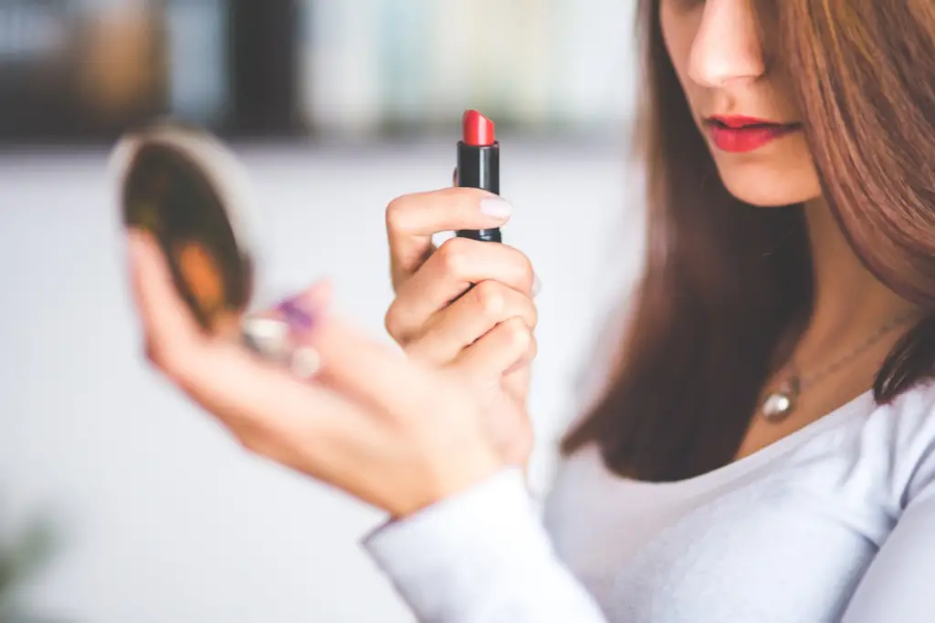 Photo of a woman holding a compact mirror to her face to apply makeup