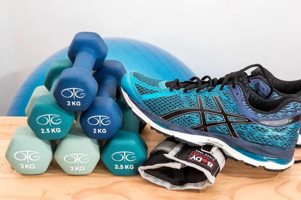 This photo shows fitness equipment including dumbbells, running shoes, an exercise ball stacked on a table.
