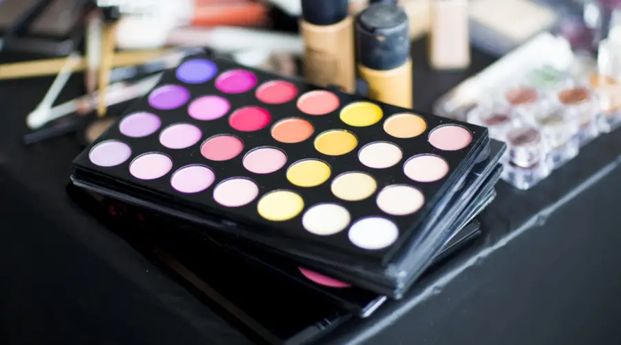 photo of a makeup tray with various colors and makeup brushes plus other beauty products around the makeup.