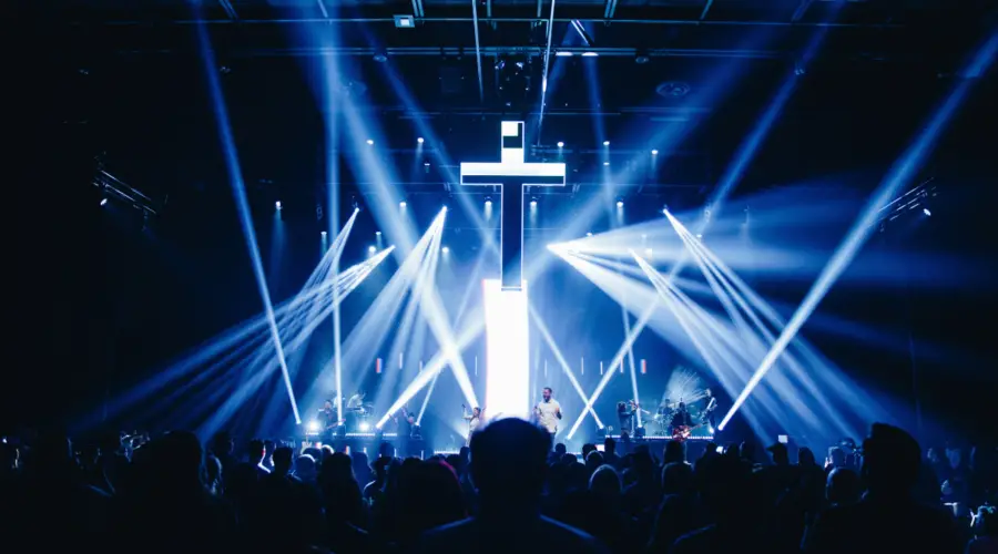 This is a photo of a cross/crucifix hanging above a stage at a Christian rock concert with stage lighting around it