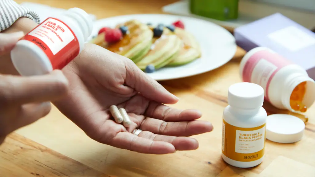 The photo shows a person's hand with two capsules that's just been tipped out of a small container with a label that reads "hair, skin and nails dietary supplement".