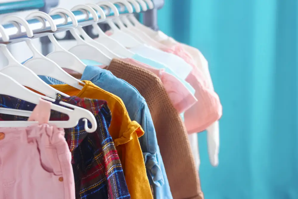 A selection of children's clothing in pastal colors hanging from coat hangers against a blue background