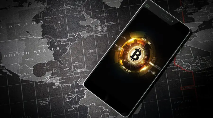 Bitcoin was the first cryptocurrency to be accepted globally and remains the dominant virtual currency around the world. This is reflected in this image showing a smartphone against the backdrop of a worldwide map. Bitcoin affiliate programs operate globally in support of borderless transactions.
