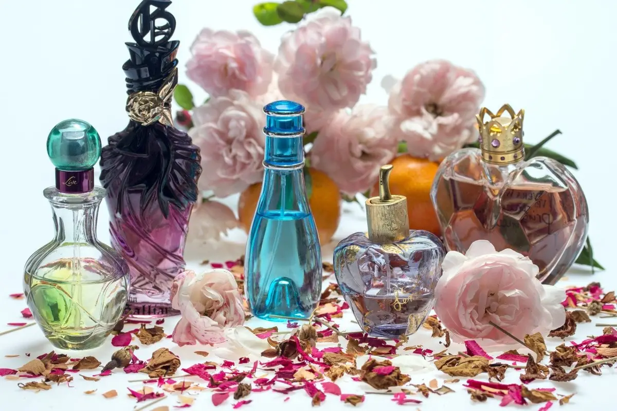 The image shows a variety of perfume decanters displayed with florals and petals representing some of the natural ingredients used in perfumes.
