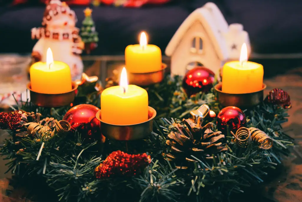 The image shows four lit yellow candles in a decorative wreath used as part of a festive table display.